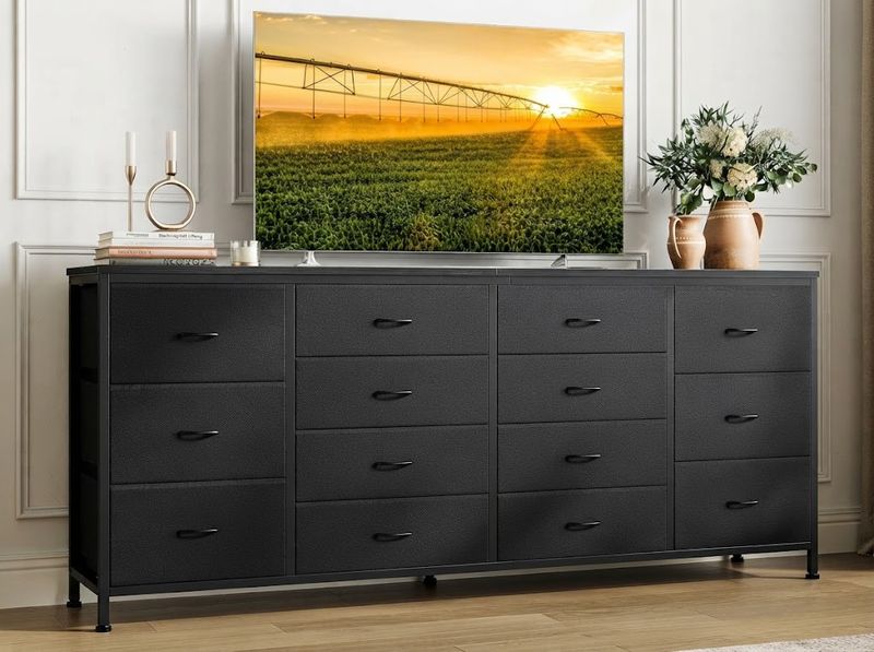 Anti-tip strap being fastened behind a black fabric dresser in a nursery